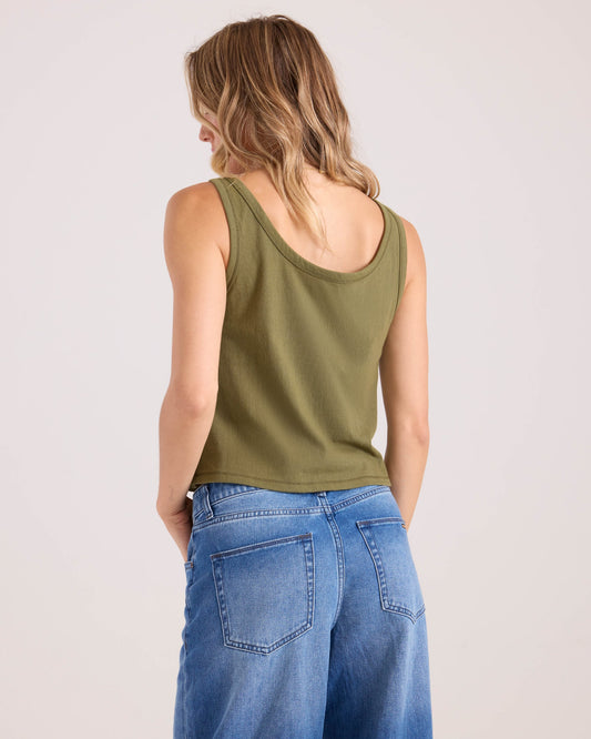 A woman with wavy, shoulder-length blonde hair is seen from behind wearing the Volcom Women's 91 Tank in olive green and high-waisted blue jeans against a plain light background.