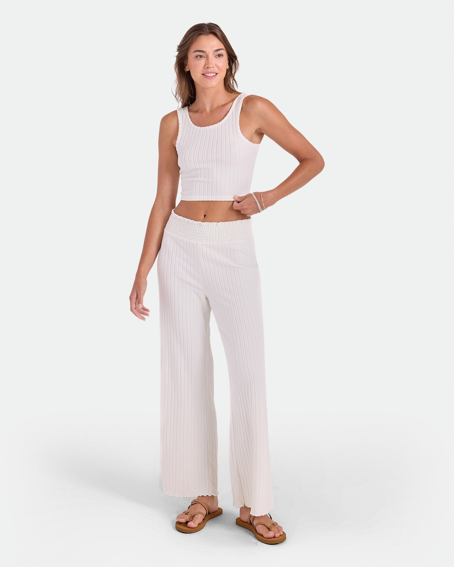 A woman smiles in a Volcom Women's Lounge Bra Tank paired with wide-leg pants and sandals, posing against a plain white background—an essential everyday outfit.