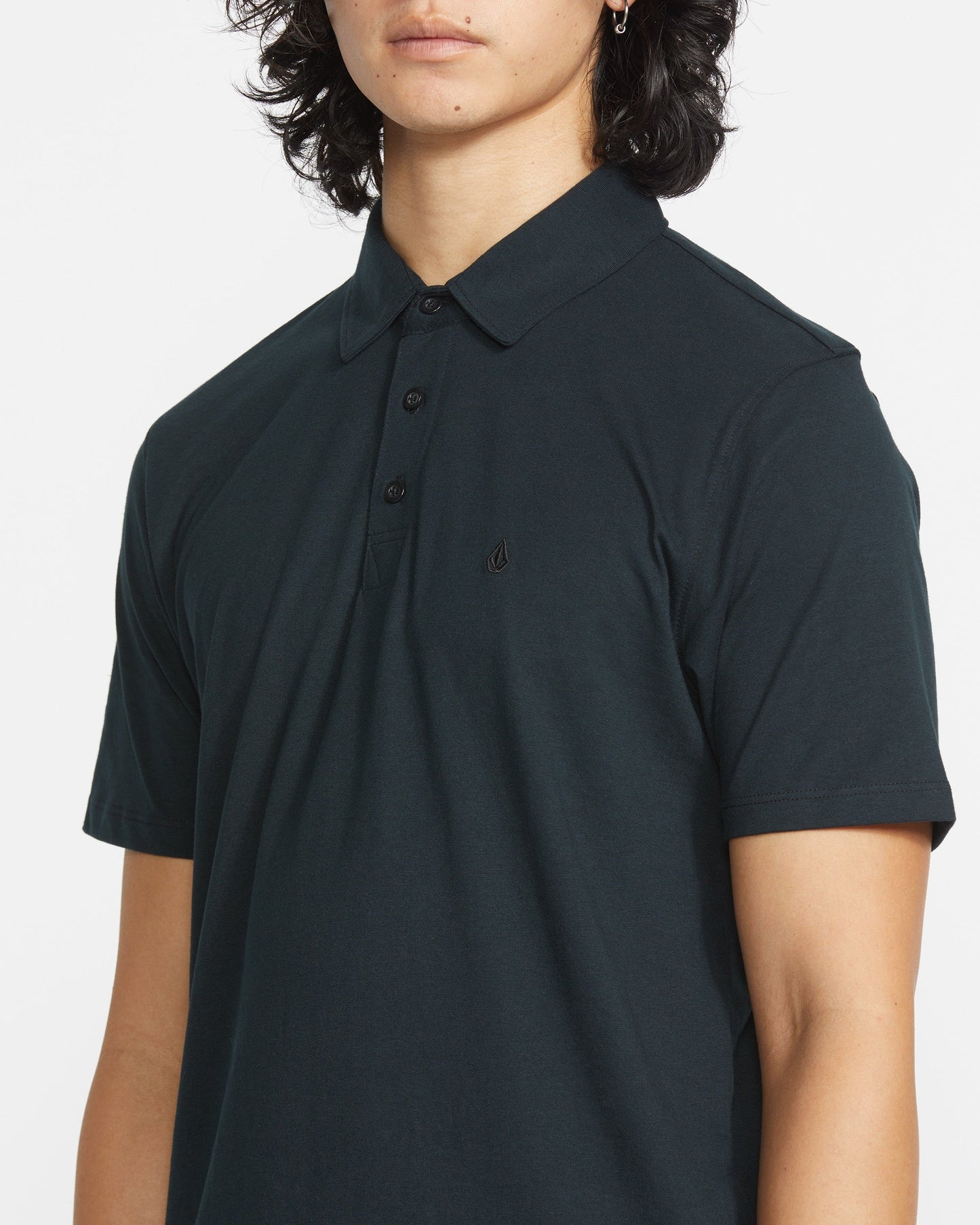 A man with medium-length dark hair wears the Volcom Men's Wowzer Polo Short Sleeve Shirt, featuring a small chest logo, shown from the shoulders up against a plain white background.