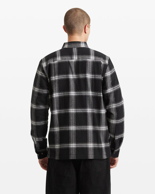 A person with short hair is shown from the back against a plain white background, wearing the Volcom Men's Wilderstone Long Sleeve in a black and white plaid pattern with black pants.