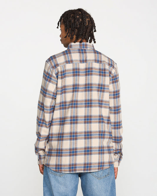 A person with short dreadlocks is shown from the back, wearing the Volcom Men's Caden Plaid Long Sleeve Shirt in beige, blue, and brown, paired with light blue jeans against a plain white background.