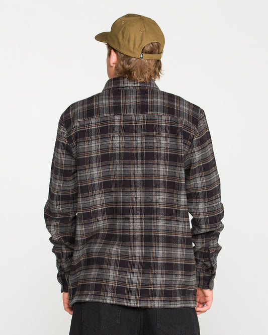 A person wearing a brown cap and a dark Volcom Men's Johnstone Long Sleeve Shirt is facing away from the camera against a plain white background.