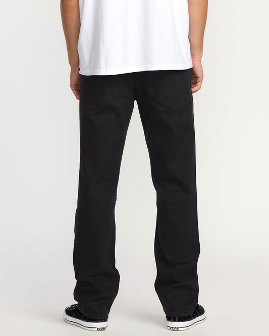 A person faces away, wearing a white T-shirt, black-and-white sneakers, and Volcom Men's Volcom Entertainment Pennywise Denim Pants, against a plain light backdrop.