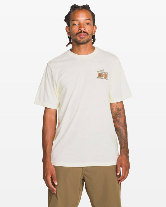 A person with dreadlocks and tattoos on their right arm wears the Volcom Men's Breathe Deep Short Sleeve Tee in heather, featuring a small left chest graphic, paired with khaki shorts, standing against a plain white background.
