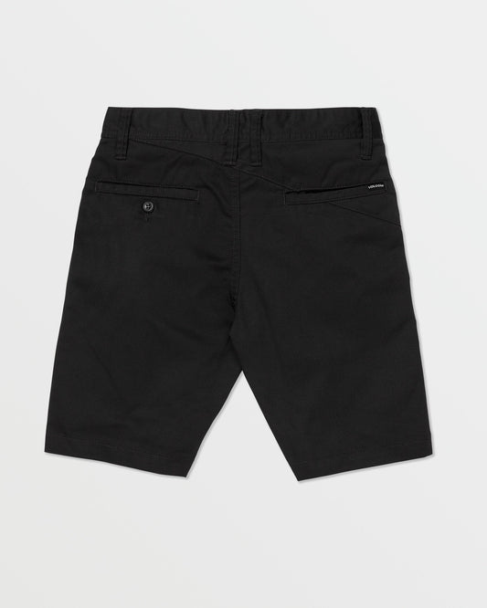 The Volcom Kids' Frickin Chino Shorts 16" are black, knee-length, shown from the back with a modern fit, belt loops, two rear pockets (one buttoned), and a black Volcom label above the right pocket. Shorts are laid flat on a white background.