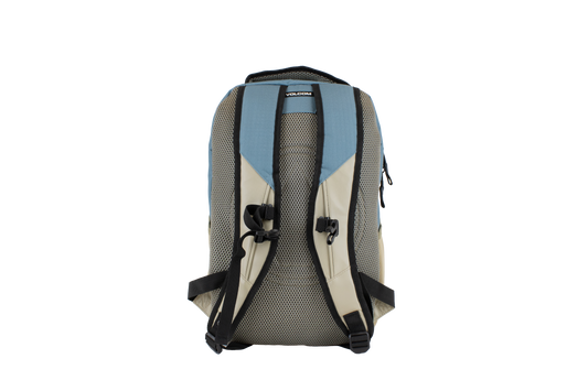 The Volcom Men's Grindstone Skate Backpack in beige and blue is shown from the back, featuring ergonomic black straps with mesh padding for comfort. A sturdy top handle and a visible Volcom brand label are present, and the backpack includes a padded laptop sleeve for added convenience.