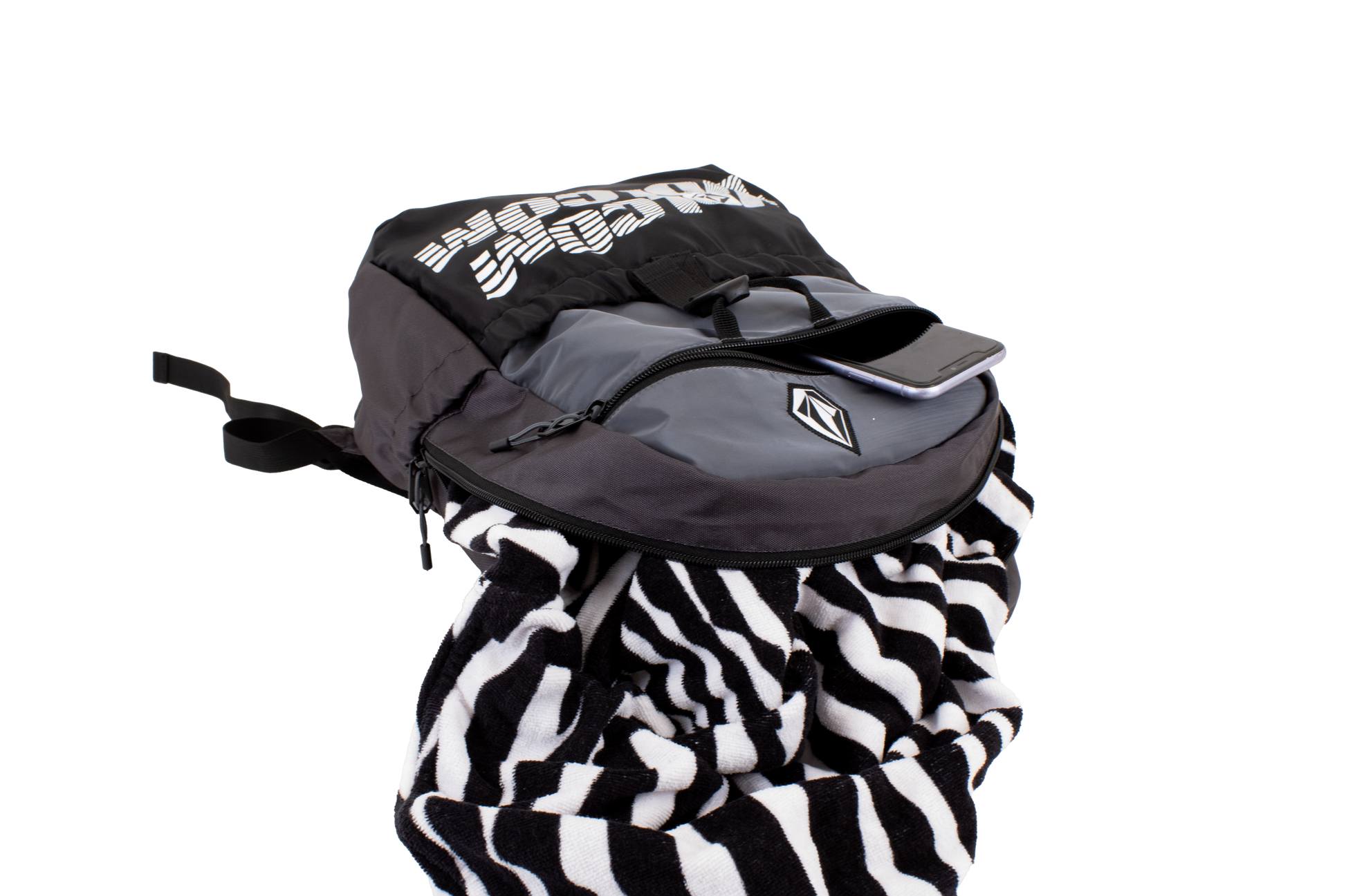 A Volcom Men's Summer School lightweight black and gray backpack, shown on a plain white background, features a convenient laptop sleeve, with a phone in the front pocket and a black-and-white striped towel partially tucked inside.