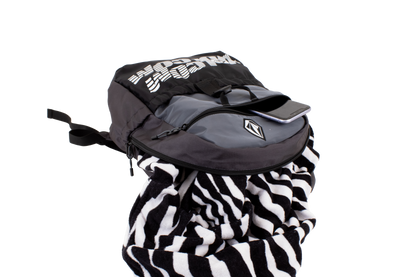 A Volcom Men's Summer School lightweight black and gray backpack, shown on a plain white background, features a convenient laptop sleeve, with a phone in the front pocket and a black-and-white striped towel partially tucked inside.
