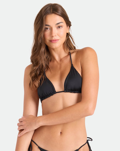 A woman with long brown hair models the Volcom Women's Simply Seamless Triangle bikini top in black, posing against a plain light gray background and looking at the camera with a slight smile.