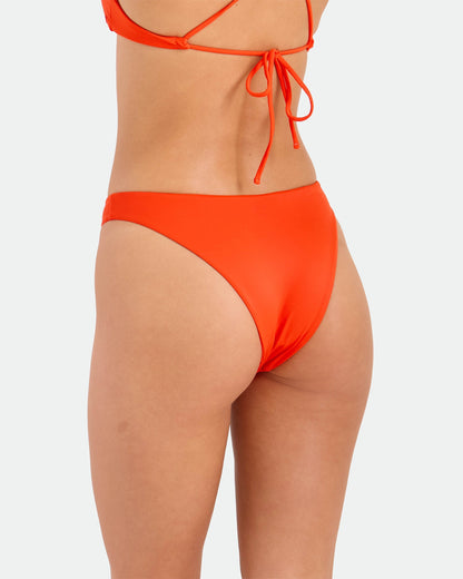 A woman is shown from the waist down, side and back, wearing the Volcom Women's Simply Seamless Midrise Skimpy bikini bottom with cheeky coverage and a matching top, set against a plain light background.