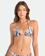 A woman with long brown hair models the Volcom Women's Hibiscus Diamond Reversible Triangle Top with adjustable ties and matching bottoms in a black and white floral print, standing against a plain background and smiling at the camera.
