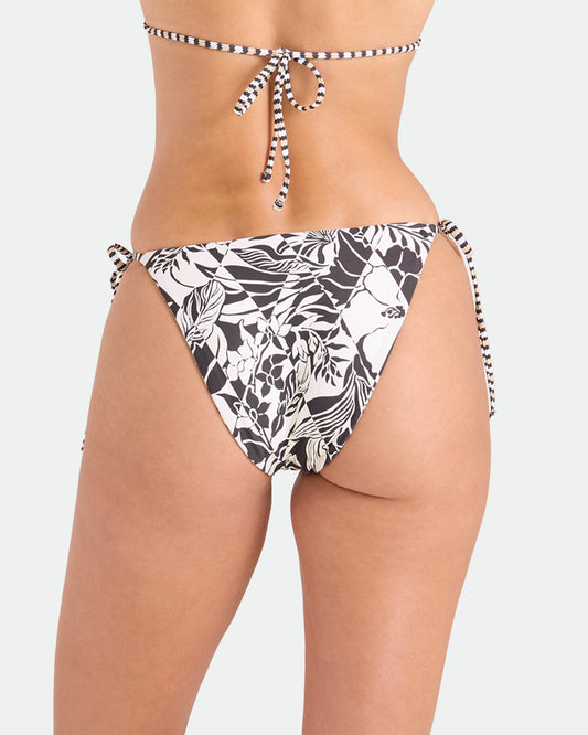A woman is shown from the back wearing Volcom's Women's Hibiscus Diamond Tie Side Full Reversible Bikini Bottom in a black and white tropical leaf print with side ties, paired with a matching bikini top, set against a plain light background.