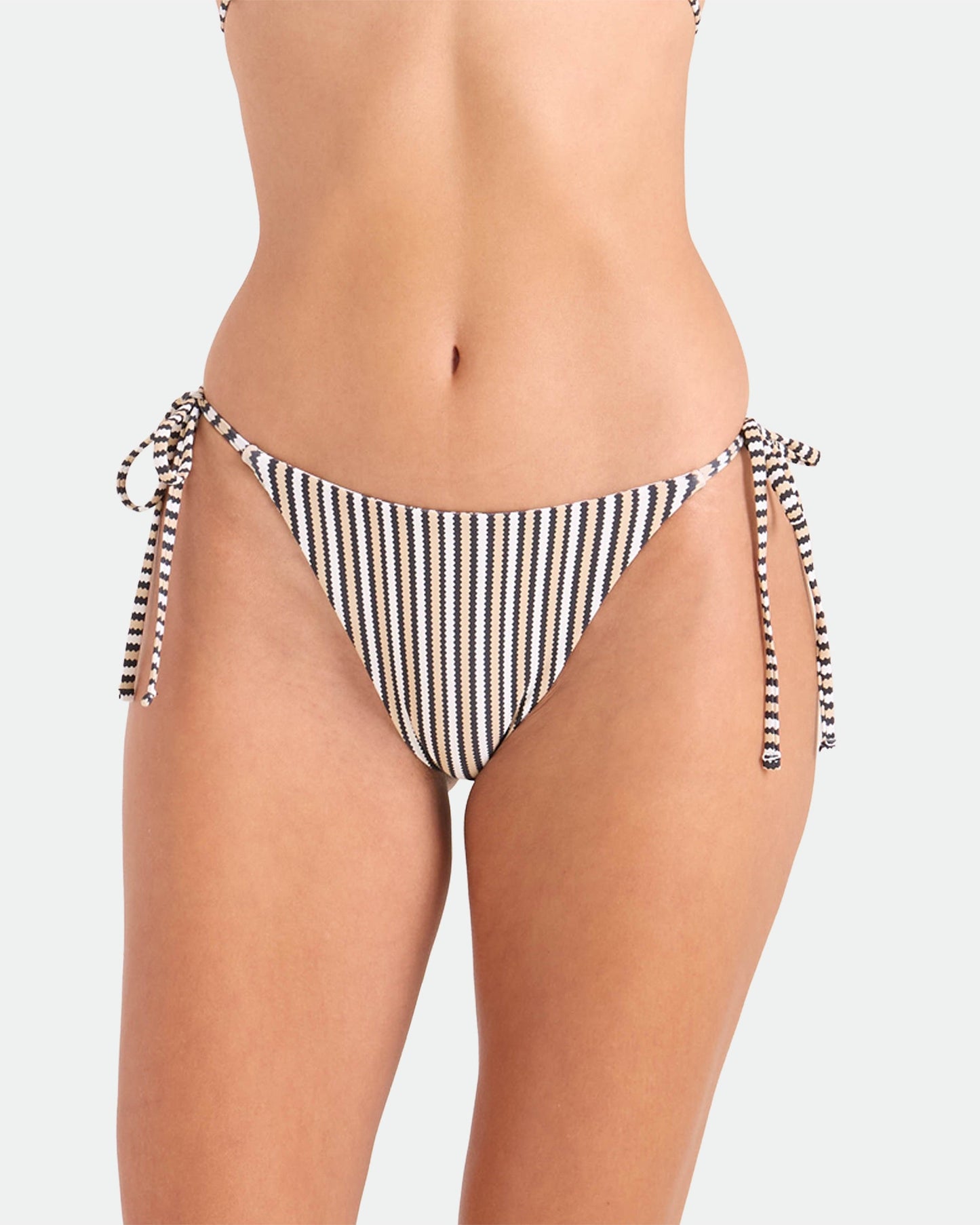 A person models the Volcom Women's Hibiscus Diamond Tie Side Full Reversible Bikini Bottom, made from recycled nylon, in black and white against a plain light background. The image is cropped to show the torso and upper thighs.