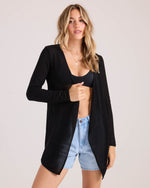 A woman poses confidently in the Volcom Women's Lived In Go Go Wrap, layered over a black bikini top and light blue denim shorts, set against a plain light background.