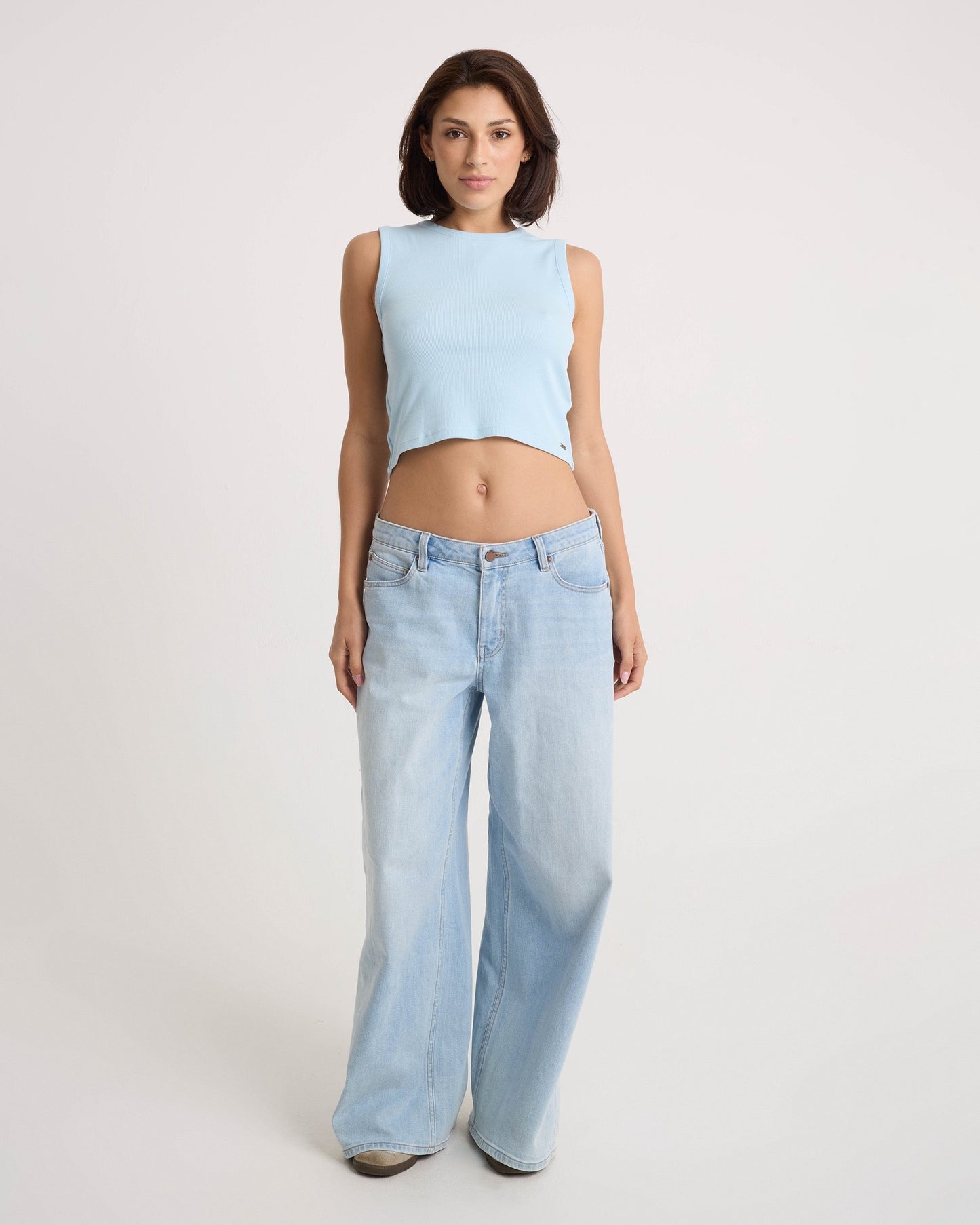 A woman faces forward against a plain light background, wearing the Volcom Women's Mary Mack Tank in light blue and loose-fitting light blue jeans.