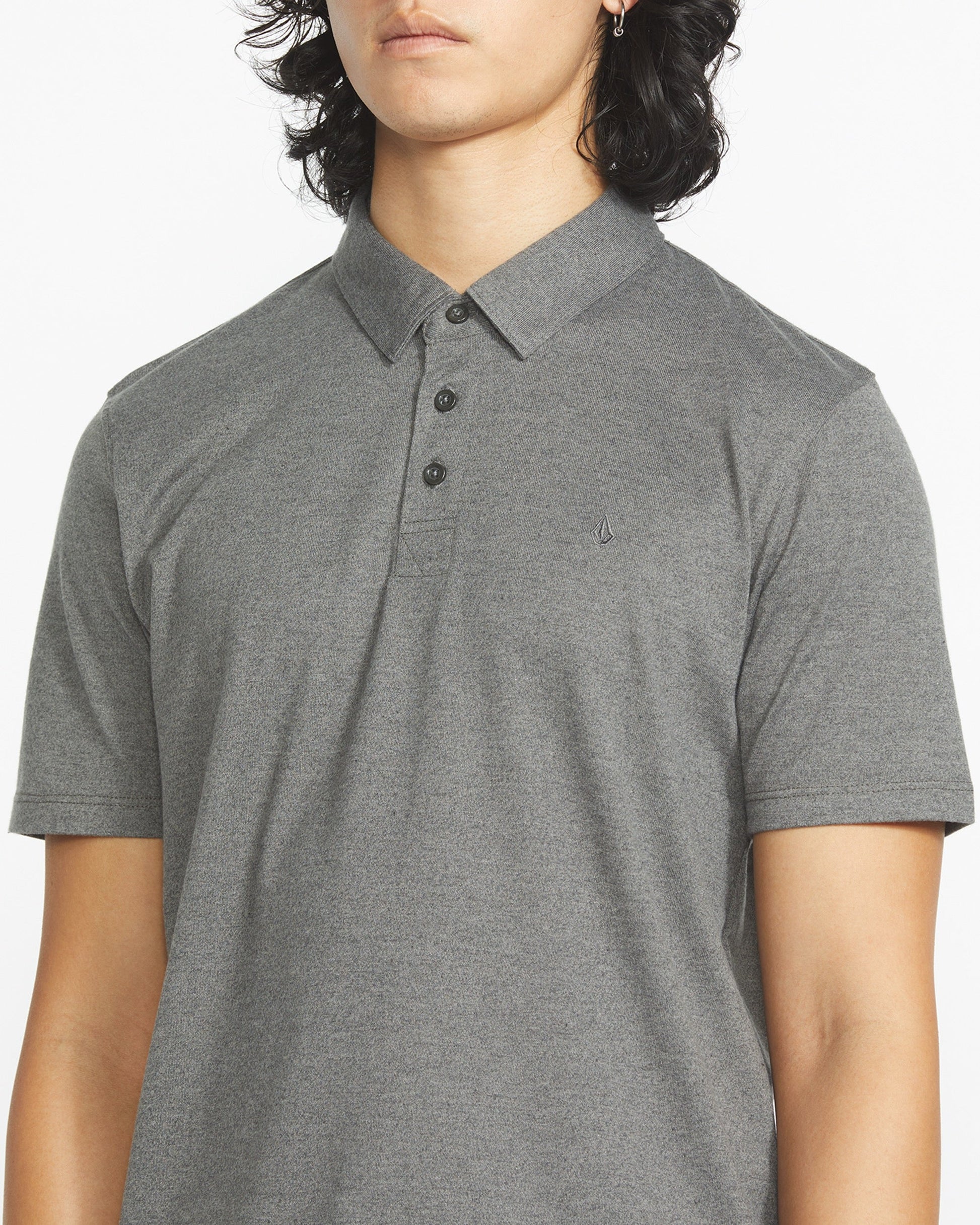 A person wears the Volcom Men's Wowzer Polo Short Sleeve Shirt in light gray, a modern fit cotton-poly blend with three buttons and a small chest Stone logo embroidery, shown from shoulders to waist.