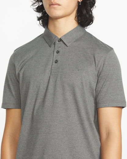 A person wears the Volcom Men's Wowzer Polo Short Sleeve Shirt in light gray, a modern fit cotton-poly blend with three buttons and a small chest Stone logo embroidery, shown from shoulders to waist.