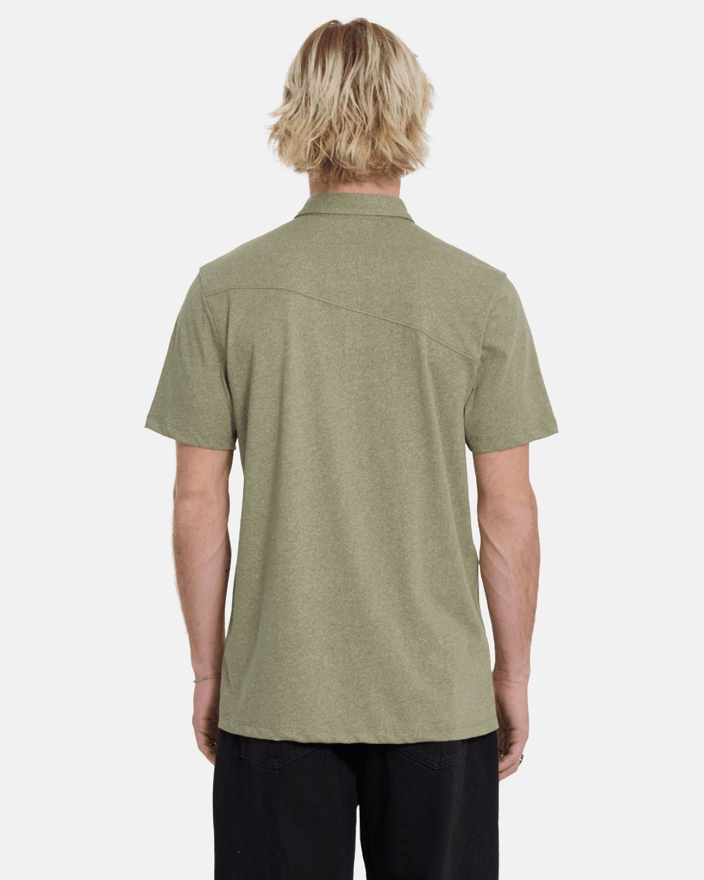 A person with light blonde, wavy hair is seen from behind wearing the Volcom Men's Wowzer Polo Short Sleeve Shirt in olive green and black pants against a plain, light background.