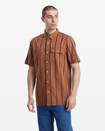 A man with short hair wears the Volcom Men's Whitworth Short Sleeve shirt, featuring vertical jacquard stripes and 100% cotton fabric, with blue jeans, standing against a plain white background.