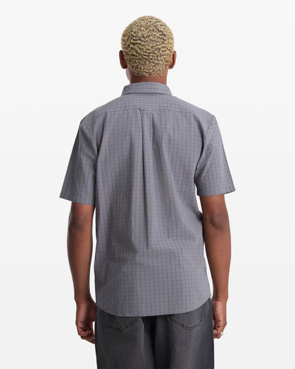 A person with short, light-blond curly hair is seen from behind, wearing the Volcom Men's Brewster Short Sleeve shirt and dark pants against a plain white background.