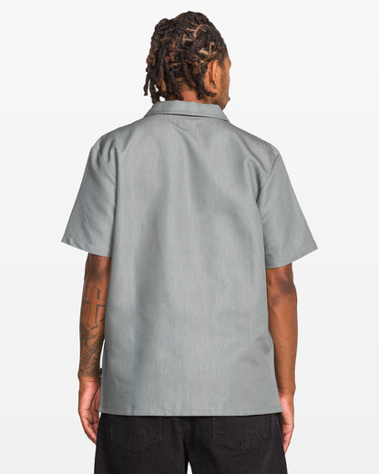 A person with short dreadlocks, seen from behind, wears the Volcom Men's Otis Stone Short Sleeve Tee and black pants against a plain white background.