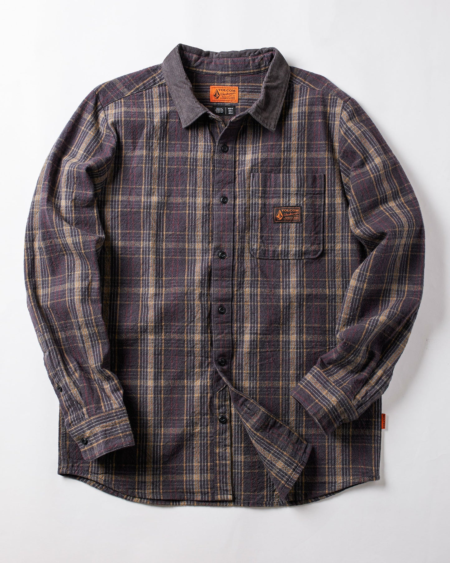 The Volcom Men's Stonevise Plaid Long Sleeve is a workwear-style flannel shirt with purple, gray, and beige plaid, chest pocket, small orange label, and button-up front. Displayed flat on a white background.