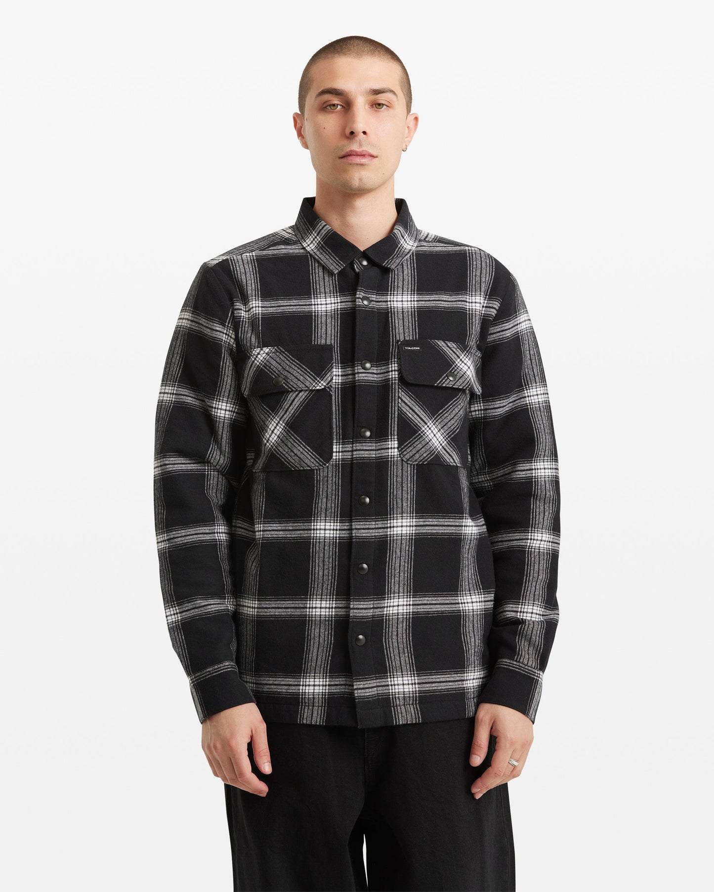 A person with short hair wears the Volcom Men's Wilderstone Long Sleeve shirt in classic black and white cotton with two chest pockets, standing against a plain white background.