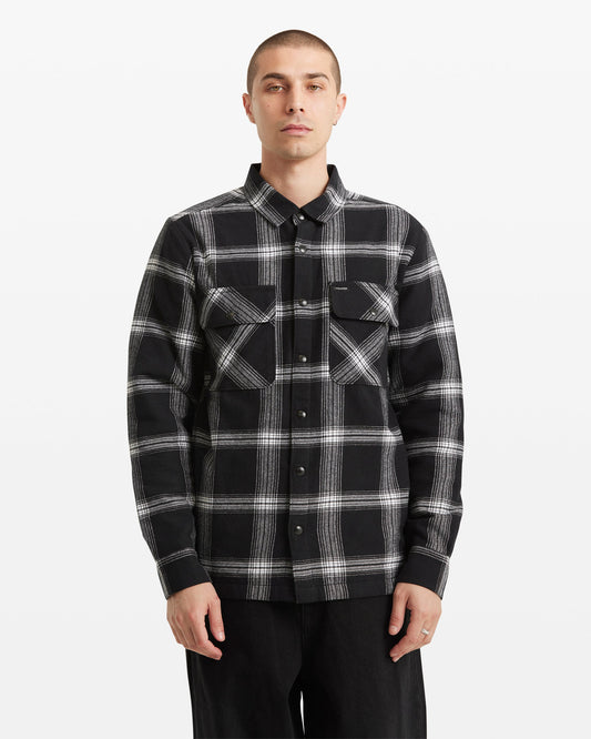A person with short hair wears the Volcom Men's Wilderstone Long Sleeve shirt in classic black and white cotton with two chest pockets, standing against a plain white background.
