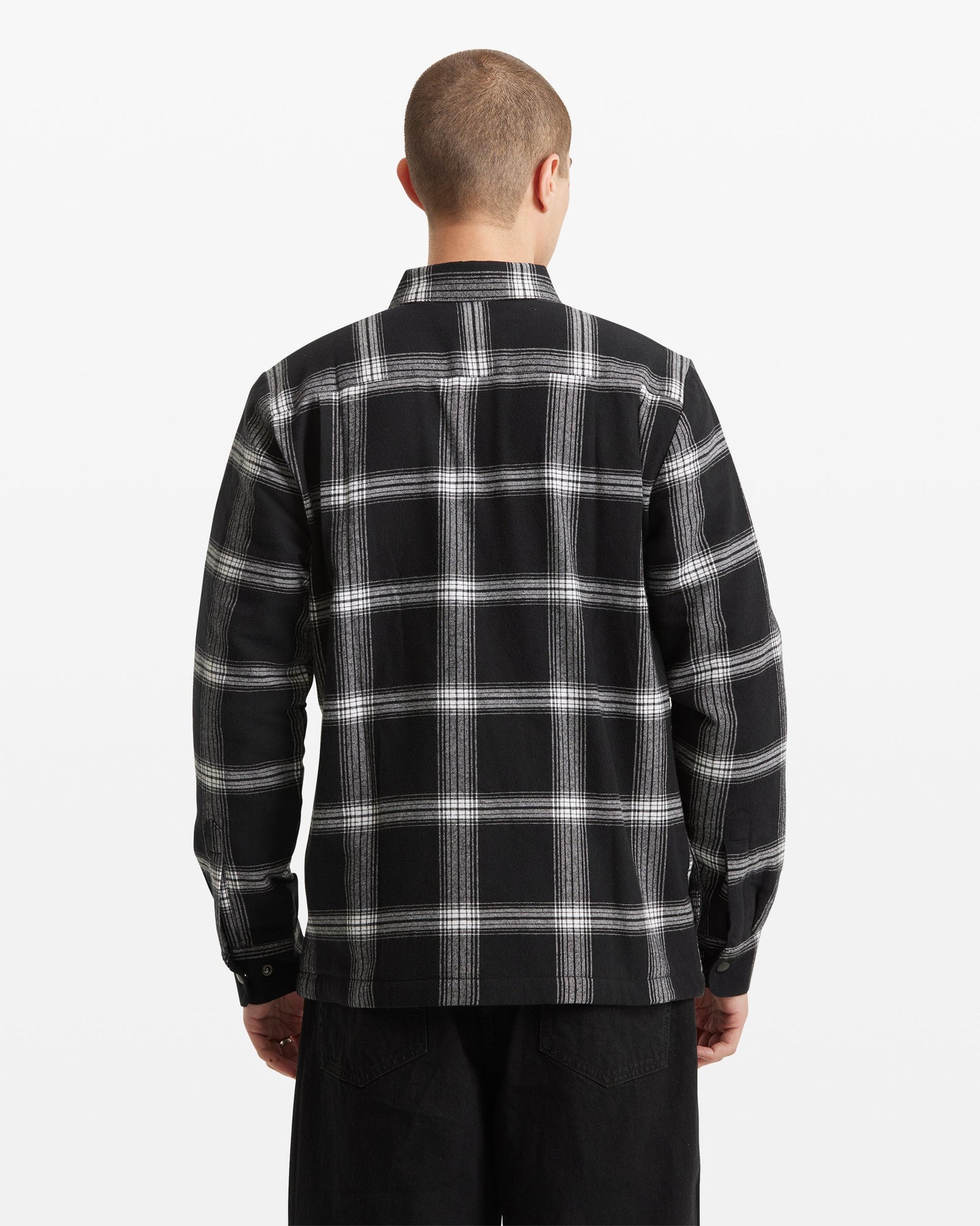 A person with short hair is shown from the back against a plain white background, wearing the Volcom Men's Wilderstone Long Sleeve in a black and white plaid pattern with black pants.