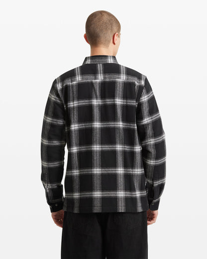 A person with short hair is shown from the back against a plain white background, wearing the Volcom Men's Wilderstone Long Sleeve in a black and white plaid pattern with black pants.