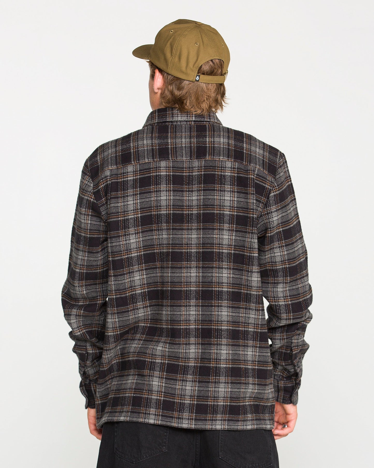 A person wearing a brown cap and a dark Volcom Men's Johnstone Long Sleeve Shirt is facing away from the camera against a plain white background.