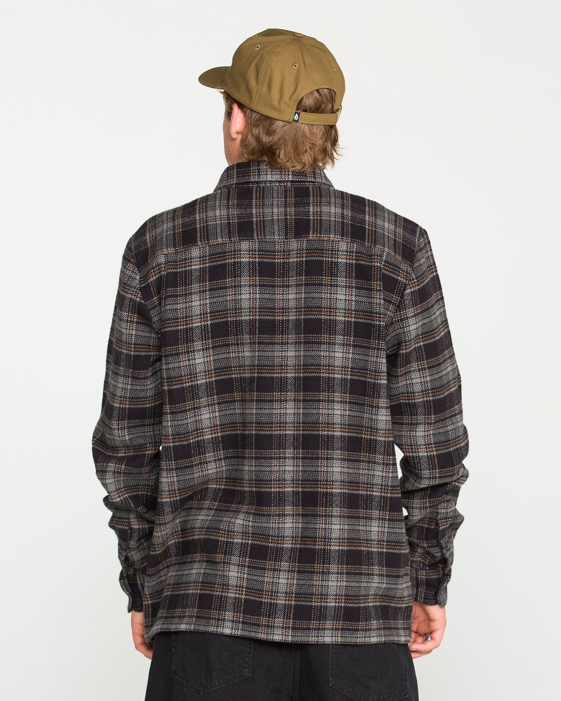A person wearing a brown cap and a dark Volcom Men's Johnstone Long Sleeve Shirt is facing away from the camera against a plain white background.