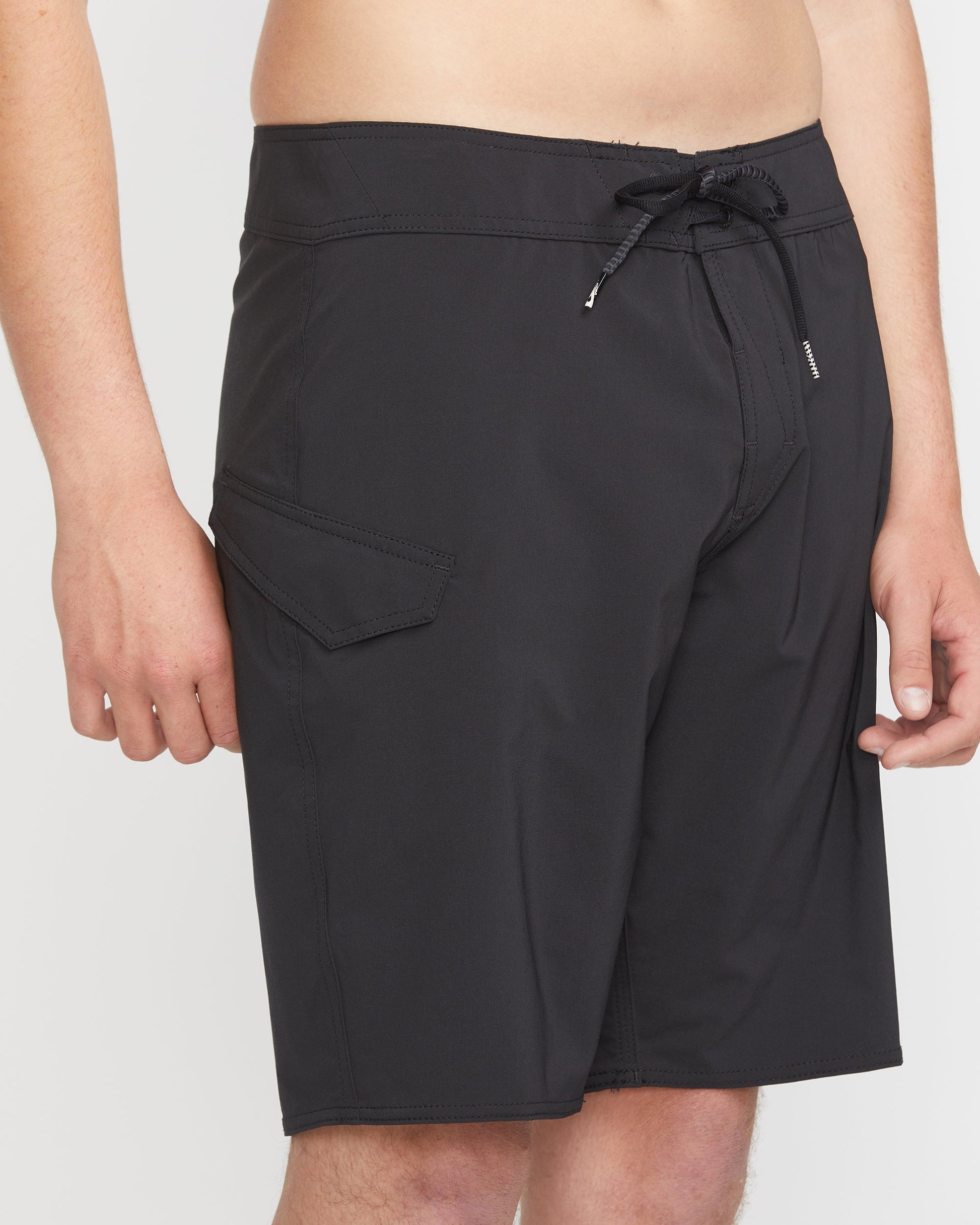 A man models Volcom's Men's Lido Solid Mod 20 black board shorts, featuring a drawstring waist and side flap pocket, standing against a plain white background. Only his torso and upper legs are shown.