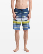 A person stands barefoot, shown from the waist down against a plain white background, wearing Volcom Men's Quarta Dissolve Mod 20 swim trunks featuring blue, white, and yellow stripes with a drawstring waist.