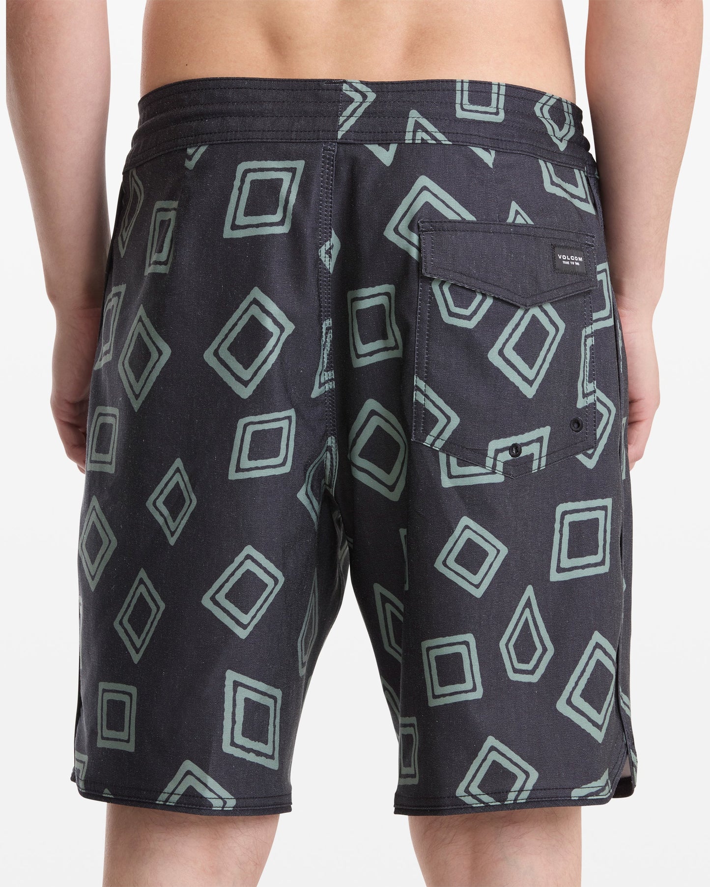 A person is shown from the back wearing Volcom Men's Contact Scallop Stoney 19 black shorts with a green geometric square pattern and a buttoned flap pocket on the right side.