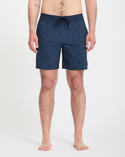 A man stands barefoot against a white background, wearing Volcom Men's Psyche Cotton Stoney 17 navy swim trunks with a drawstring waist. His arms rest at his sides, and only his lower body is fully visible.