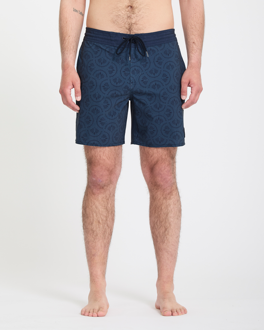 A man stands barefoot against a white background, wearing Volcom Men's Psyche Cotton Stoney 17 navy swim trunks with a drawstring waist. His arms rest at his sides, and only his lower body is fully visible.
