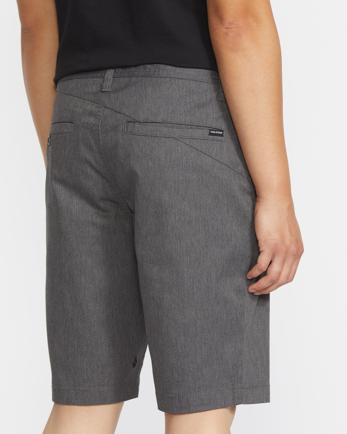 A person in a black shirt and Volcom Men's Frickin Modern Stretch Shorts stands facing away, highlighting the shorts' breathable fabric, two back pockets, and a small Volcom tag above the right pocket.