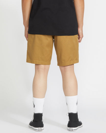 A person stands facing away from the camera wearing a black t-shirt, Volcom Men's Frickin Elastic Waist Shorts, white crew socks, and black sneakers against a plain white background.