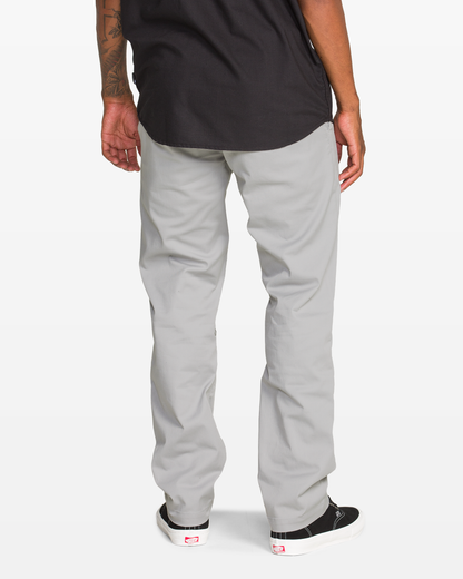 A man, seen from behind with only his lower half visible, wears Volcom Men's Frickin Modern Stretch Pants made from recycled polyester, paired with a black shirt and black-and-white sneakers.