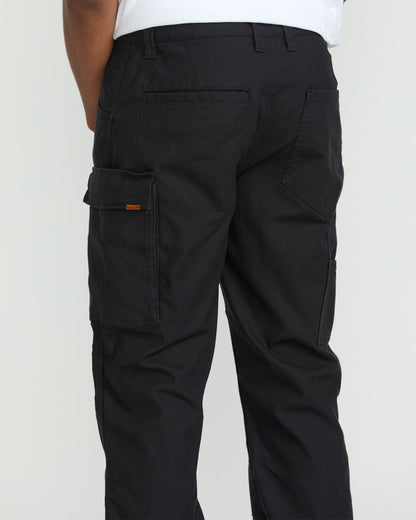 A person wearing Volcom Men's Caliper II Relaxed Work Pants in black stretch canvas with multiple pockets, including a left-leg cargo pocket, and a white shirt; shown from the waist down and behind.