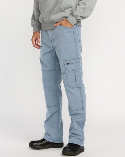 A person models Volcom Men’s Gage Work Pants in light blue, paired with a gray hoodie and black shoes against a white background. One hand is in their pocket, and their face is not shown.
