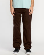 A person wears Volcom Men's Solver 5 Pocket Slub Pants and black sneakers with white soles, standing against a plain white background. Only their lower torso and legs are visible.