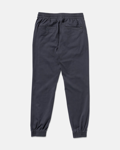 The Volcom Men's Frickin Slim Joggers in dark gray are shown from the back, featuring an elastic waistband, slim fit, two back pockets (one with a button), and made from REPREVE recycled fibers on a plain white background.