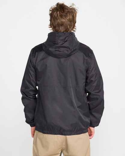 A person with light brown hair is seen from the back, wearing Volcom's Men's Ermont Jacket in black and beige pants, standing against a plain white background.