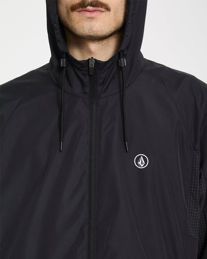 A man wears the Volcom Men's Wavern Jacket, a black zip-up hoodie with a small white Volcom logo on the chest; only the lower half of his face is visible.