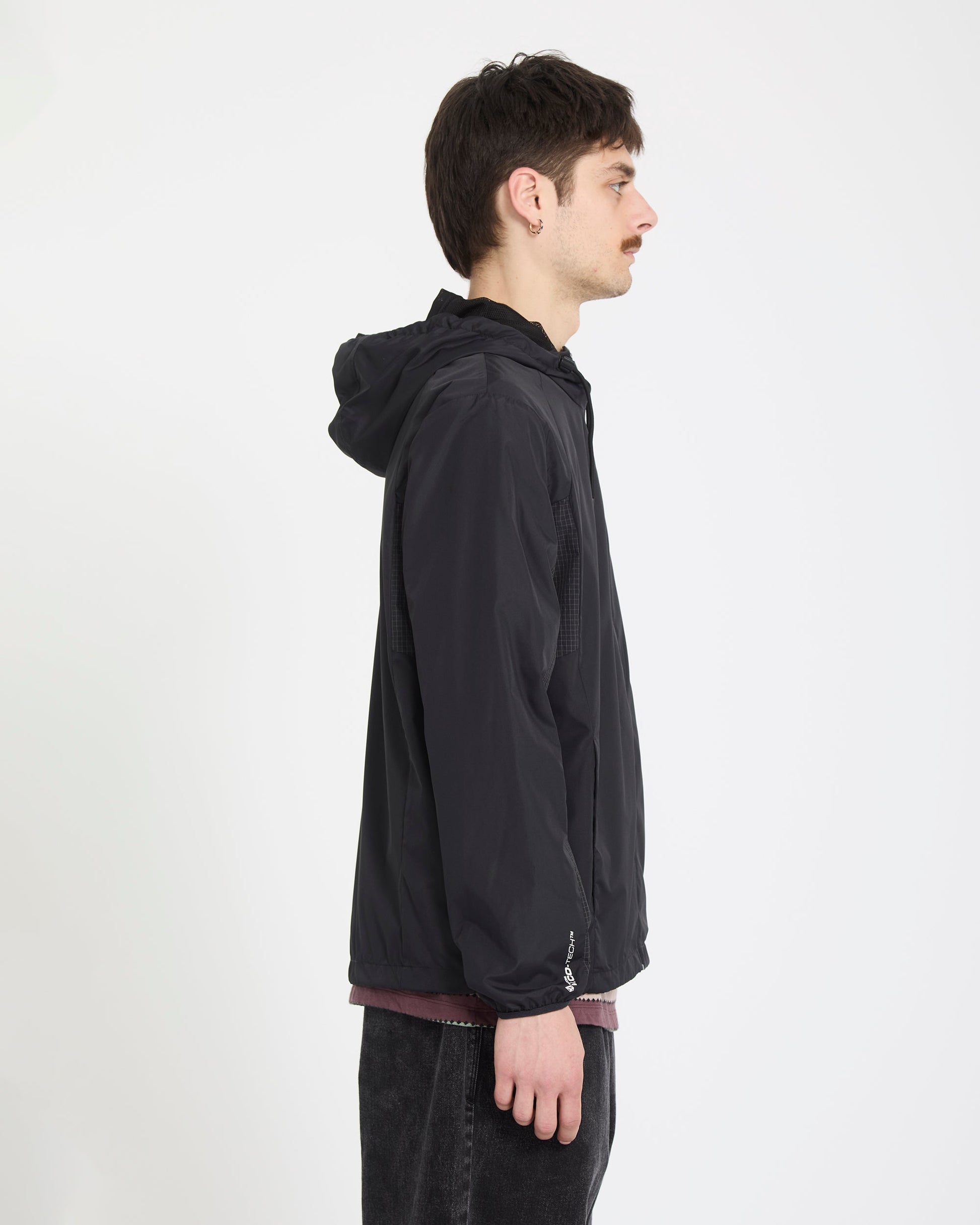 A man with short dark hair and a mustache stands in profile against a white background, wearing the Volcom Men's Wavern Jacket over a maroon shirt and dark pants.