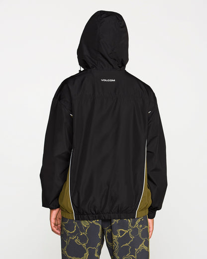 A man is shown from the back against a plain white background, wearing the Volcom Men's Wavestone Jacket in black with olive side panels and patterned pants. The jacket includes a mesh-lined hood for enhanced breathability.