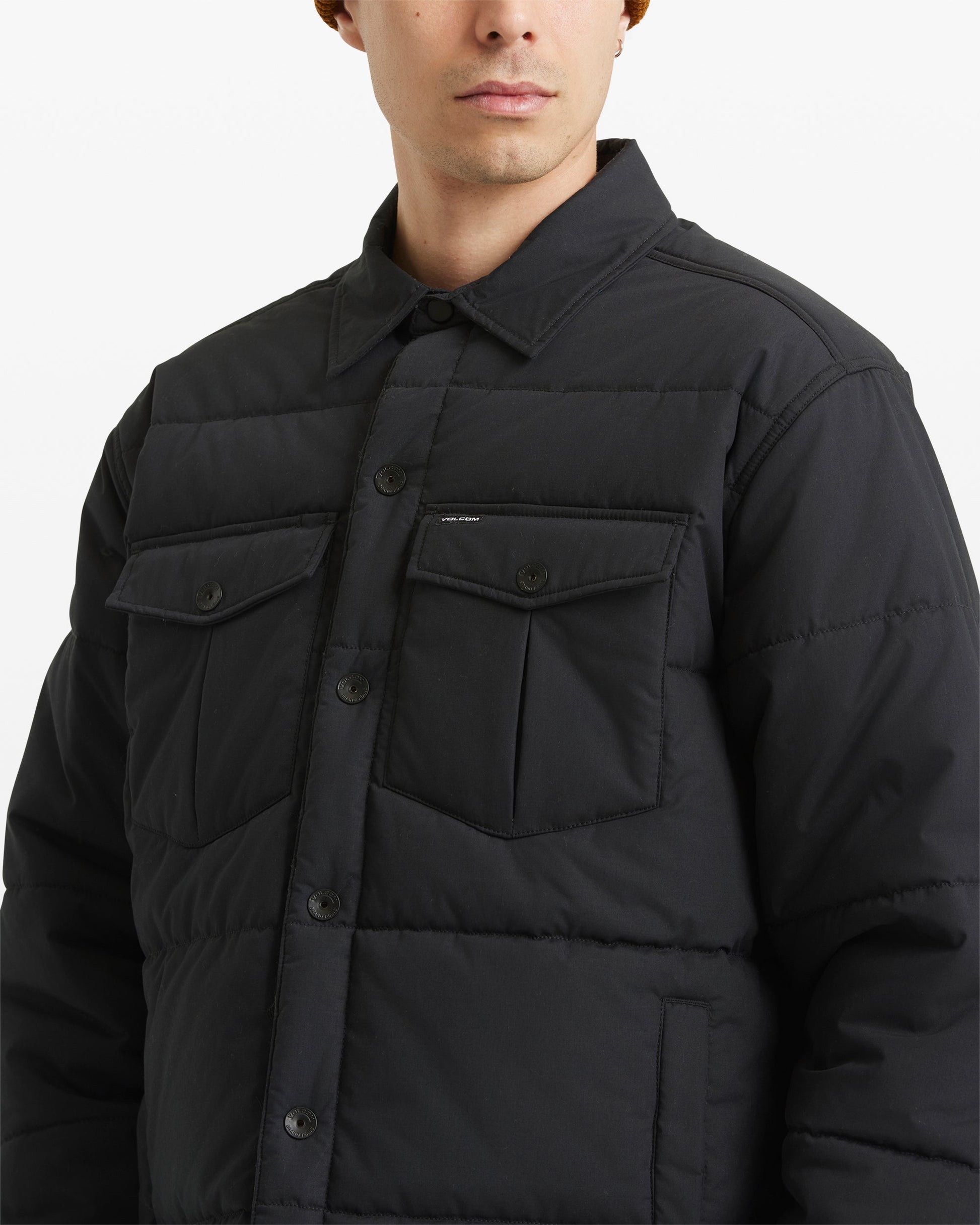 A man wearing the Volcom Men's Westmead Quilted Jacket, featuring a buttoned front and two chest pockets, is shown from the chest up against a plain white background.