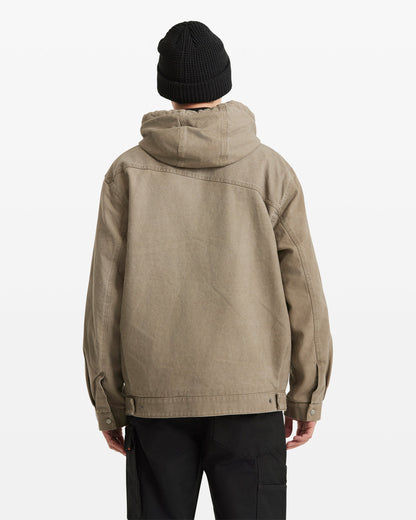 A person wears the Volcom Men's Freshdust Workwear Jacket in tan with a zip front, along with a black beanie and black pants, standing facing away from the camera against a plain white background.